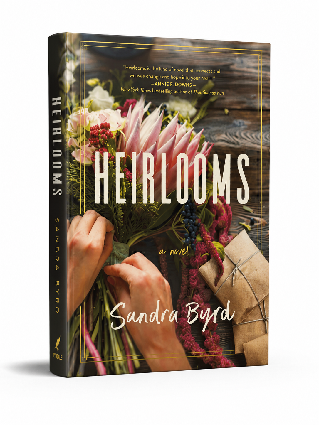 Book cover of 'Heirlooms' by Sandra Byrd with hands holding flowers and a wooden surface.